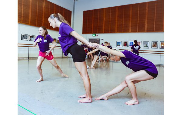 Two students practise pair work with one leaning forward holding another student who is behind her leaning back and her right leg bent straight out in front of her. To the left of them is a student is practising another jujitsu move with her right leg bent and her left leg straight behind it. She is leaning forward and has her right hand over her chest.
