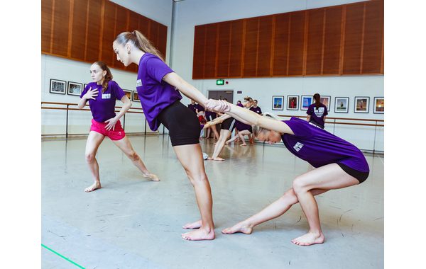 Two students practise pair work with one leaning forward holding another student who is behind her leaning back and her right leg bent straight out in front of her. To the left of them is a student is practising another jujitsu move with her right leg bent and her left leg straight behind it. She is leaning forward and has her right hand over her chest.