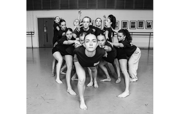 A black and white image of a group of students huddled together holding onto each other. They are looking at the camera.