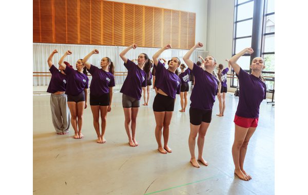 Seven students are standing in a diagonal line and have their right fists held up in the air in unity and are leaning to the left.
