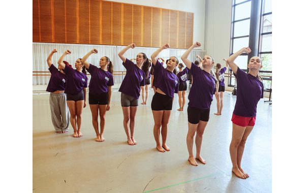 Seven students are standing in a diagonal line and have their right fists held up in the air in unity and are leaning to the left.