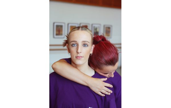 A close up of a student looking at the camera with another leaning her head on her shoulder with an arm around her.