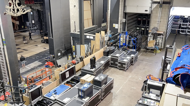 Backstage at the thatre, lots of large travel boxes are lined up and to the left we can see technicians working on the stage