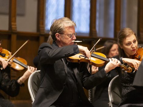 Four seated people, all dressed in black, playing the violin
