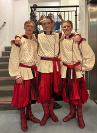Three young men stand next to each other, smiling in Russian folk-style beige and red costumes. They are stood backstage after performing in The Nutcracker.